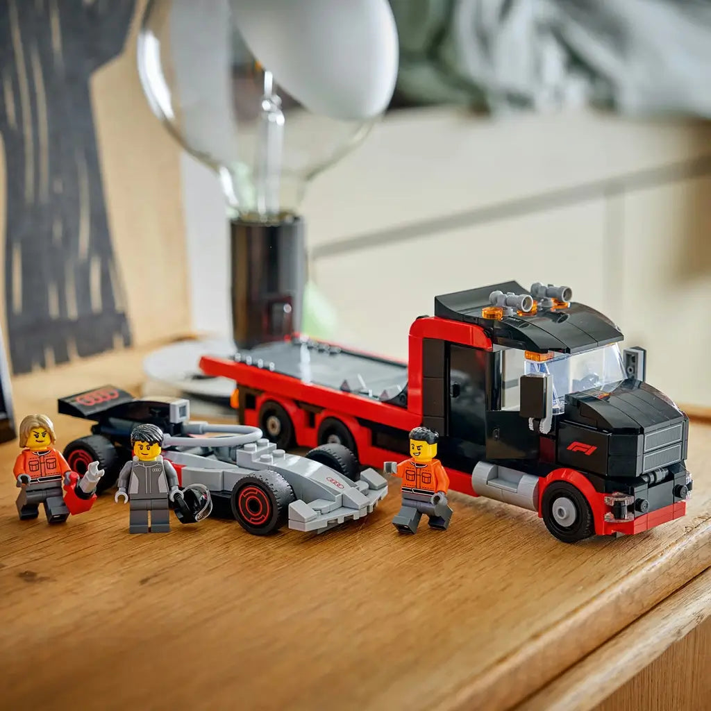 LEGO City F1 display set in red, black, and gray plastic, flatbed truck carrying race car with minifigures, completed toy scene arranged on a wooden table in a home environment.
