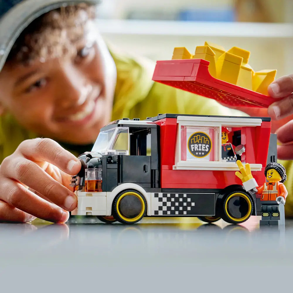 LEGO City fries food truck lifestyle builder scene featuring a child playing with the completed red food truck, lifting the fry roof and interacting with minifigures to demonstrate hands-on play.