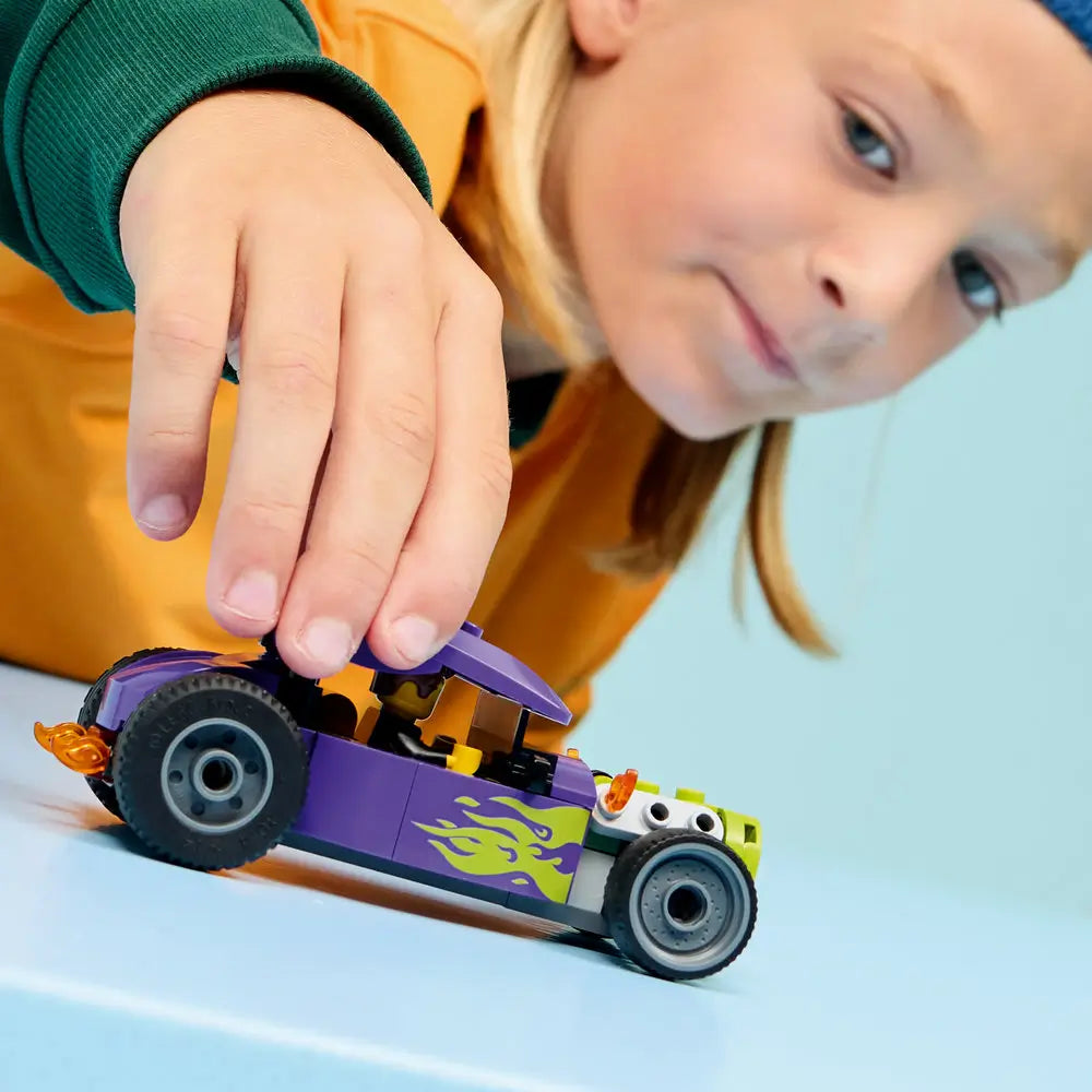 LEGO City Hot Rod lifestyle scene showing a young child pushing the completed purple and lime green hot rod toy, flame side graphics, chunky wheels, and enclosed seat on a smooth light blue tabletop.