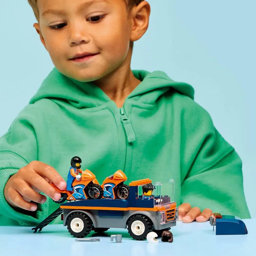 LEGO City motorcycle transporter toy played with by a child, showing hands loading orange motorcycles onto the blue transport truck during imaginative roleplay.
