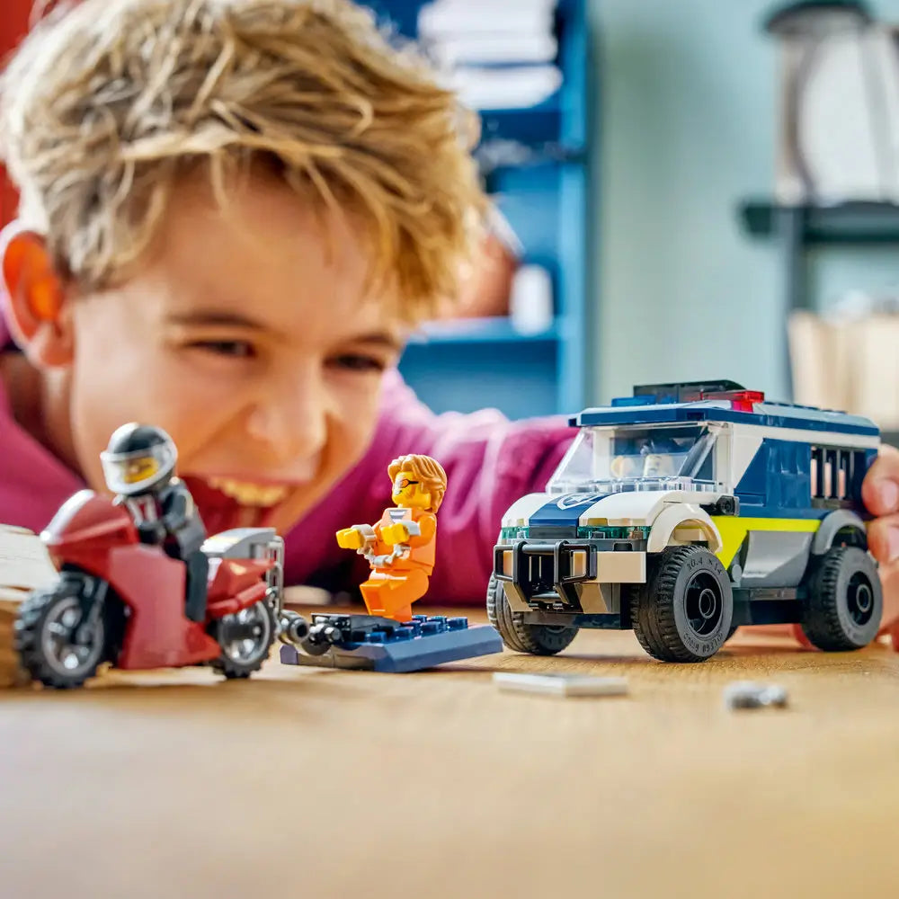 LEGO City police prisoner transport van lifestyle scene showing a smiling child playing with the dark blue and white van, red motorcycle, prisoner and police minifigures, and accessories during imaginative action play indoors.