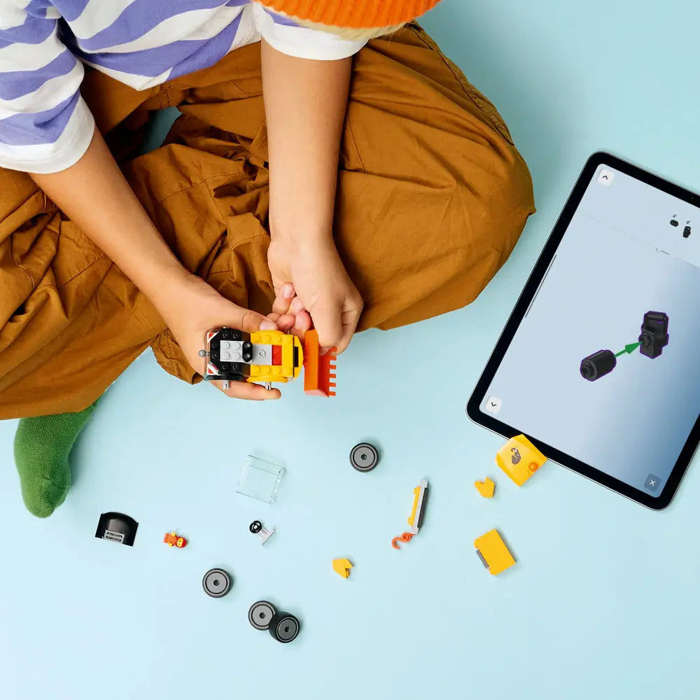 LEGO City Loader partially assembled from yellow and black plastic bricks, compact construction shape, with loose parts spread out as a child follows digital building instructions on a tablet.