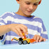 LEGO City Loader lifestyle scene showing a child pushing the completed yellow construction loader toy, clear cab, orange scoop, six-wheel design, and minifigure driver on a smooth light blue tabletop.