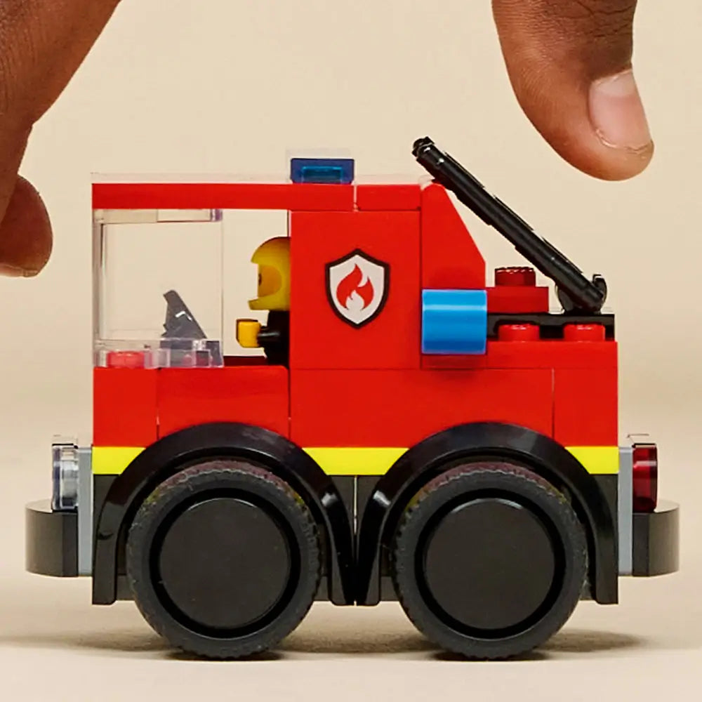 LEGO City Fire Truck fully built display model in red and black plastic bricks, enclosed cab with clear panels, roof-mounted light bar, ladder element, six wheels, and firefighter minifigure on a clean studio background.