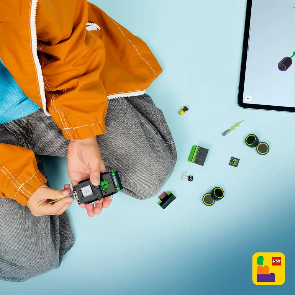 LEGO City Gaming Car building activity showing black and neon green plastic pieces, small wheels, and electronic-themed parts, assembled by a child beside a tablet displaying digital instructions on a light blue surface.