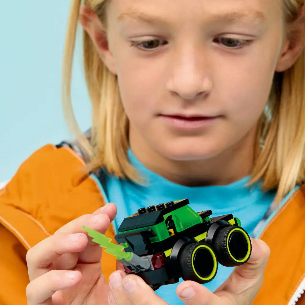 LEGO City Gaming Car lifestyle image showing a child holding the completed black and neon green gaming car toy, translucent green windshield, oversized wheels, and lightning accessory against a soft studio background.