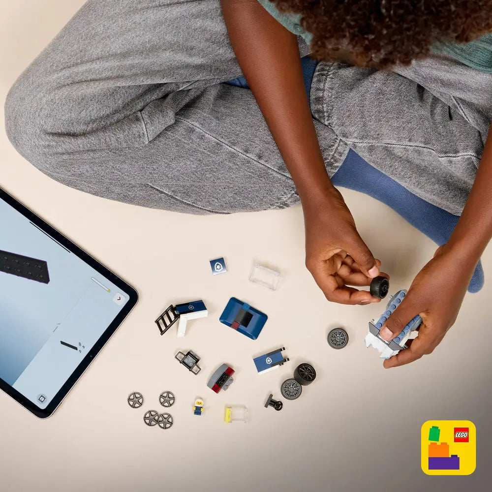 LEGO City Police Truck building activity showing dark blue, white, and black plastic pieces, wheels, roof panels, and accessories, assembled by a child beside a tablet displaying step by step digital building instructions on a light surface.