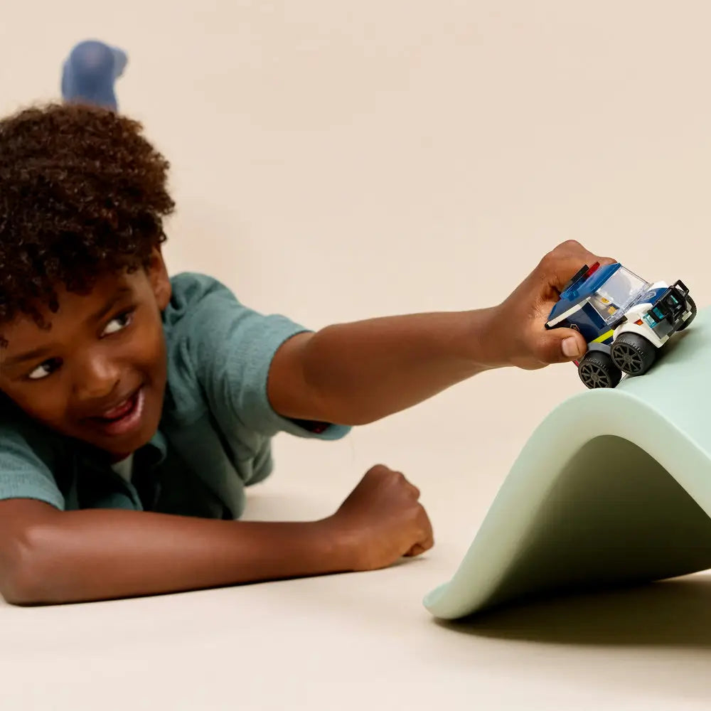 LEGO City Police Truck lifestyle scene showing a child pushing the completed dark blue and white police truck toy, chunky wheels, clear cab, roof light bar, and police minifigure during imaginative play on a smooth surface.