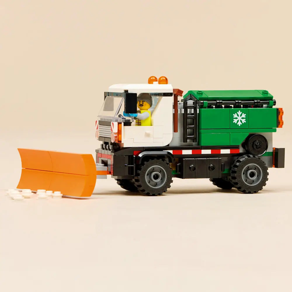 LEGO City snowplow playset fully assembled on display, showing a white and green winter service truck with an orange plow blade, chunky tires, snow pieces, and a driver minifigure in the cab.
