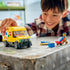 LEGO City delivery van toy played with by a smiling child, showing a yellow plastic cargo van with rolling wheels, an opening roof panel, and delivery minifigure accessories for imaginative play.