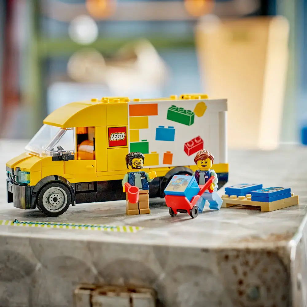 LEGO City delivery van playset fully assembled on a tabletop, featuring a yellow plastic van with an opening cargo roof, printed brick designs, minifigures, and delivery-themed accessories.