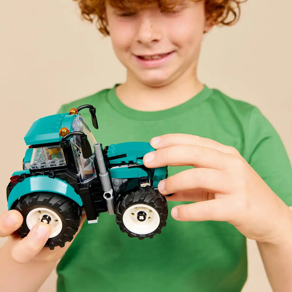LEGO City tractor toy played with by a child, showing a teal plastic farm tractor held in hands, oversized wheels, enclosed cab, and interactive features for creative roleplay.