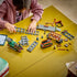 LEGO City Vintage Steam Train in green, black, red, brown, and gray plastic bricks is assembled by a child with track sections, cars, minifigures, and a tablet on a table.