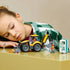 LEGO City Backhoe Loader toy in yellow and black plastic sits on a tabletop as a child plays beside two construction minifigures, a portable toilet and road sign.