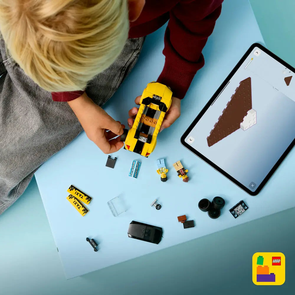 LEGO City taxi building set shown from above with yellow plastic bricks, small parts, wheels, and minifigures spread out, demonstrating assembly steps and digital instructions on a tablet over a light blue tabletop.