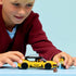 LEGO City taxi play scene with a child holding a yellow brick-built taxi car and minifigure, showing scale, rolling wheels, and imaginative roleplay against a soft light blue studio background.
