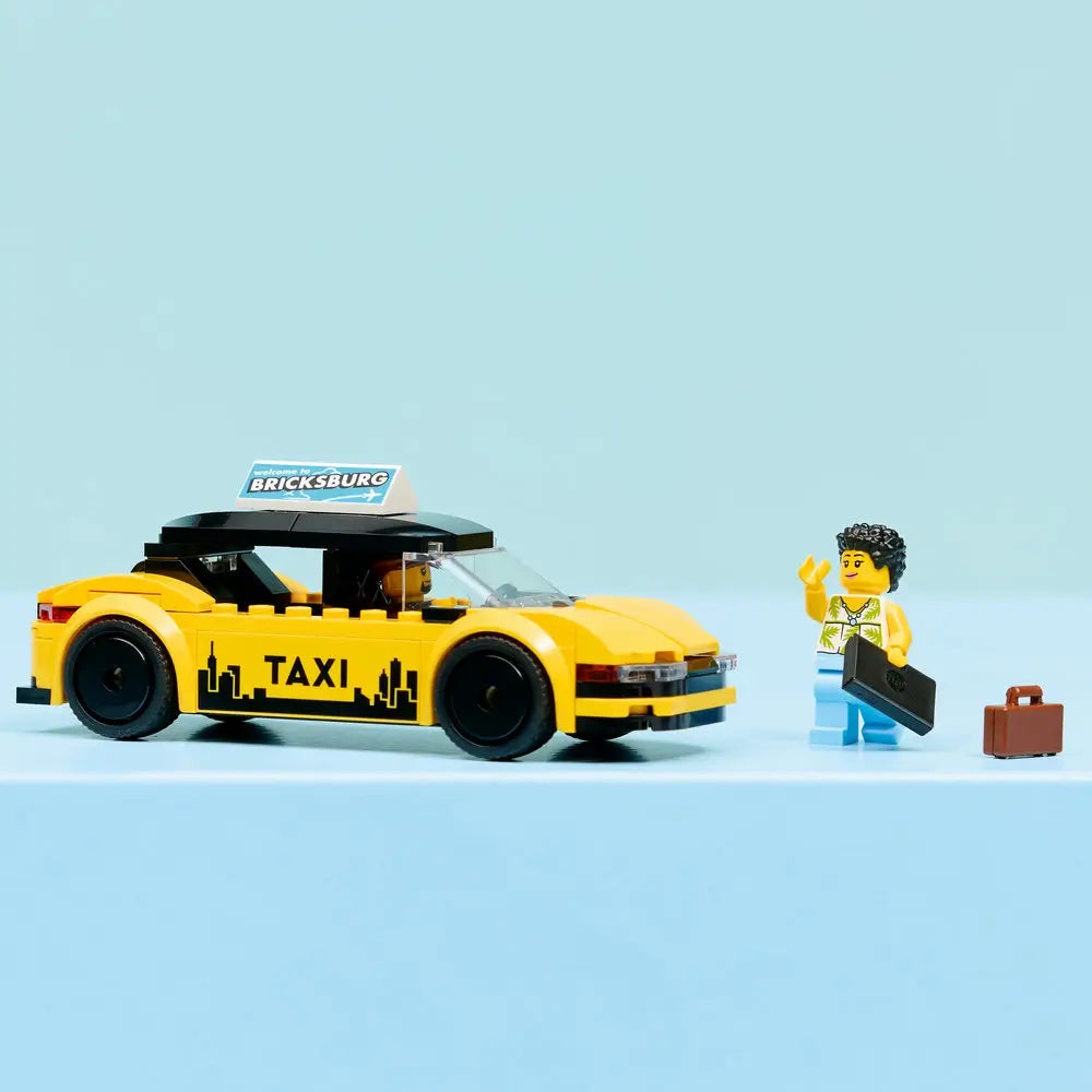 LEGO City Yellow Taxi model displayed fully built with yellow bricks, black roof, city skyline taxi graphics, and minifigure passenger, staged neatly on a light blue surface for play or display.
