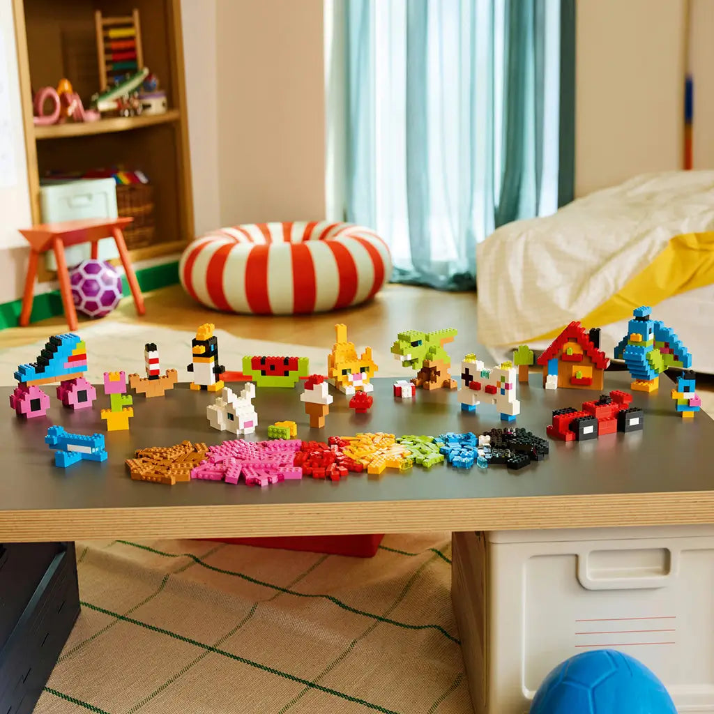 LEGO Classic colorful bricks in pink, red, yellow, green, blue, black, white, and brown form animals, vehicles, food, and a house displayed across a playroom table.