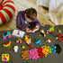 LEGO Classic colorful bricks in bright plastic colors surround a child building a white model beside a tablet, with animals, vehicles, and loose pieces on a dark table.