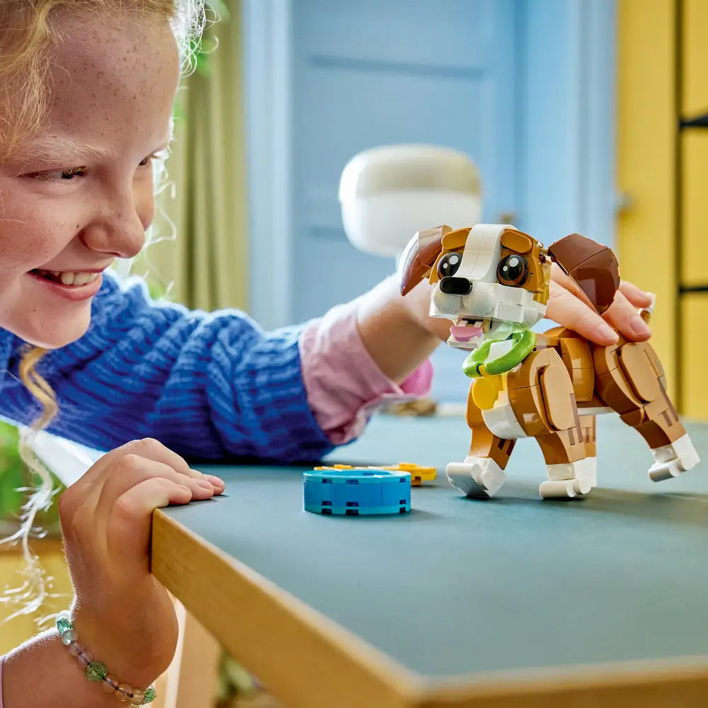 LEGO Creator puppy toy in brown and white plastic bricks as a child gently plays with the small dog figure on a table, highlighting scale, rounded shapes, and imaginative indoor play setting.