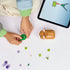 LEGO Creator hamster model being built on a tabletop, featuring tan and white plastic bricks, loose flower and leaf elements, and a partially assembled hamster positioned beside a tablet with interactive building instructions.