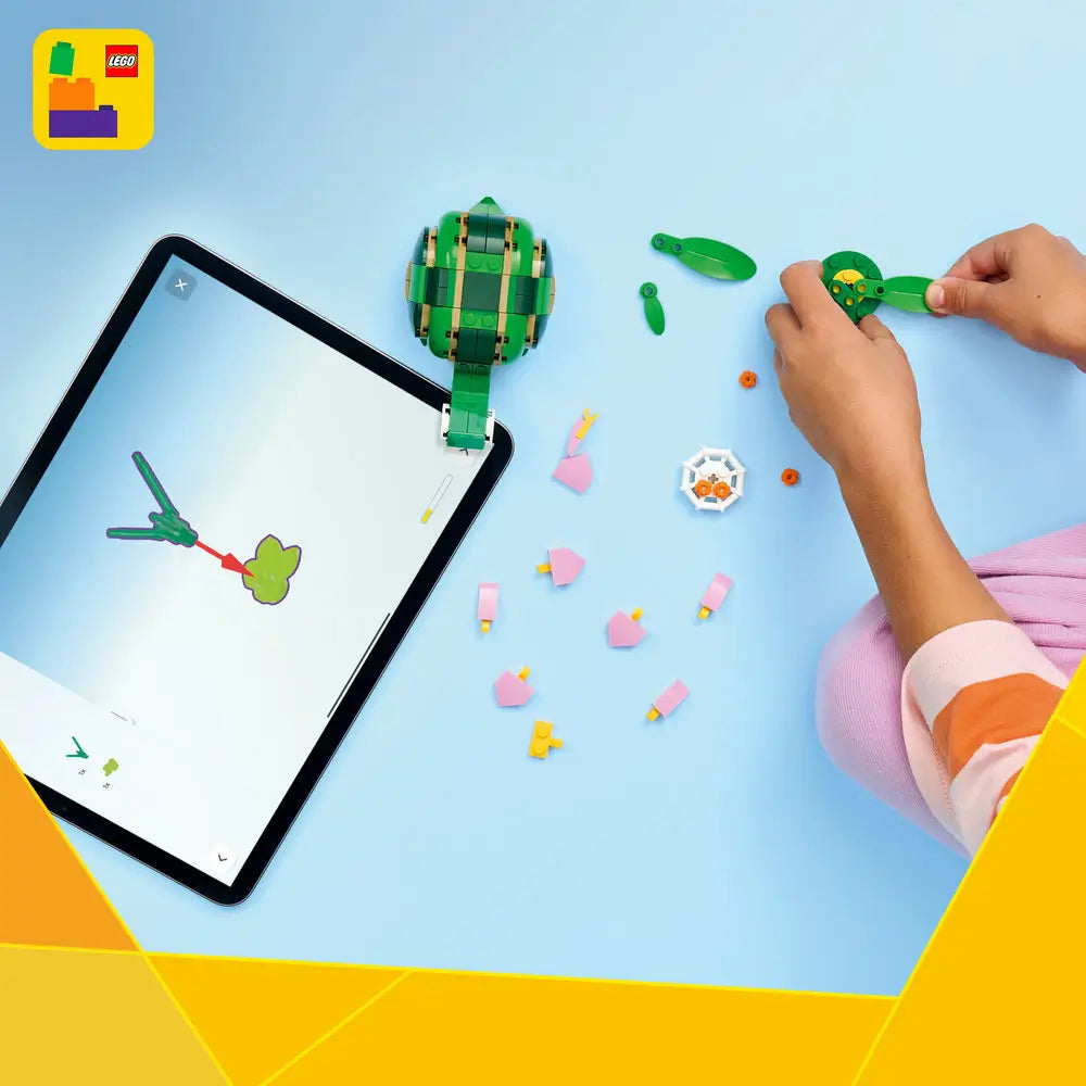 LEGO Creator turtle building set arranged on a light blue surface, showing green plastic bricks, a partially assembled turtle model, scattered leaf and flower pieces, and a tablet displaying digital step-by-step building instructions.