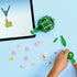 LEGO Creator turtle model being built on a tabletop, featuring green plastic bricks, loose flower and leaf elements, and a partially assembled turtle positioned beside a tablet with interactive building instructions.
