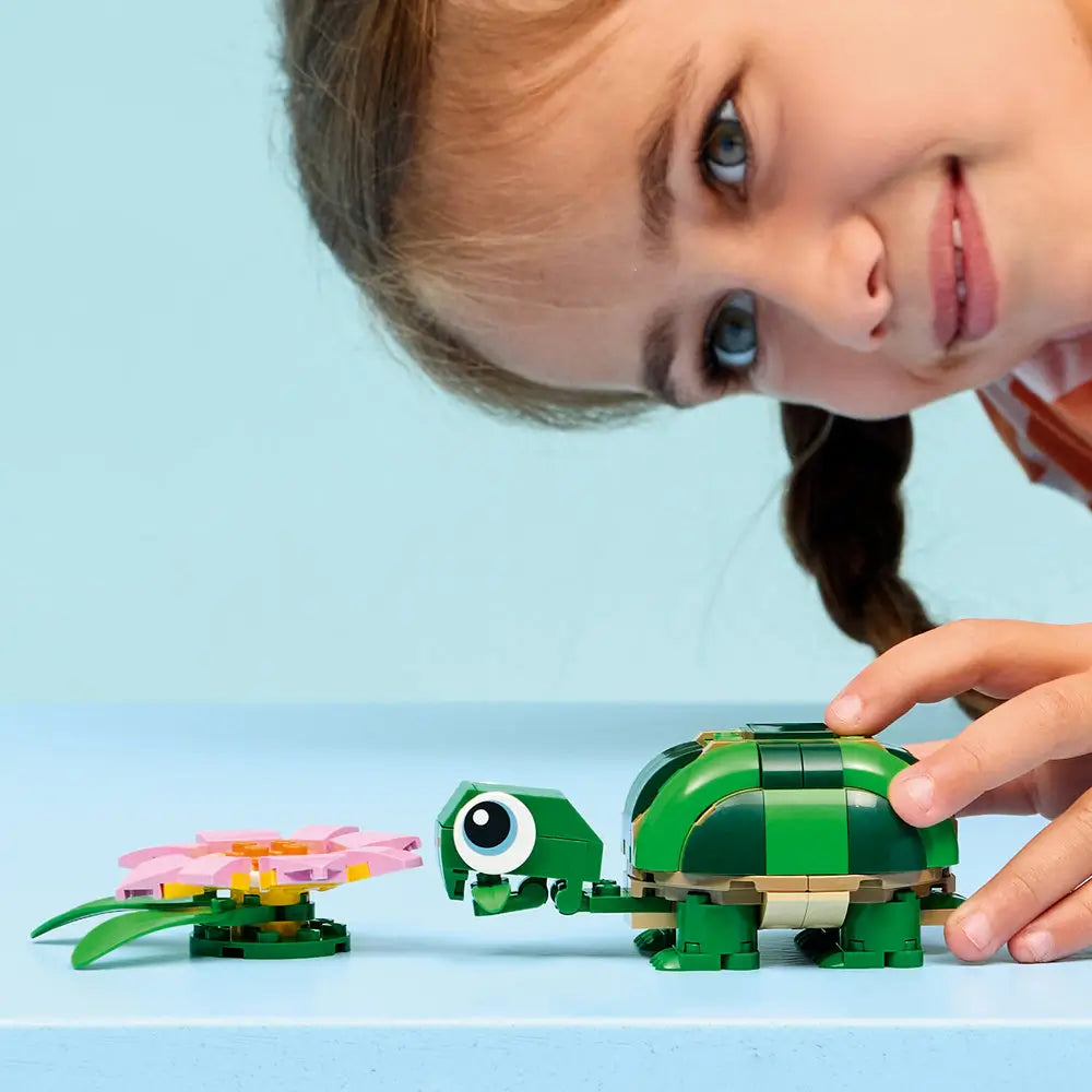 LEGO Creator turtle toy in green plastic bricks as a child gently plays with the turtle and pink water lily, highlighting scale, rounded shapes, and imaginative indoor nature-themed play.