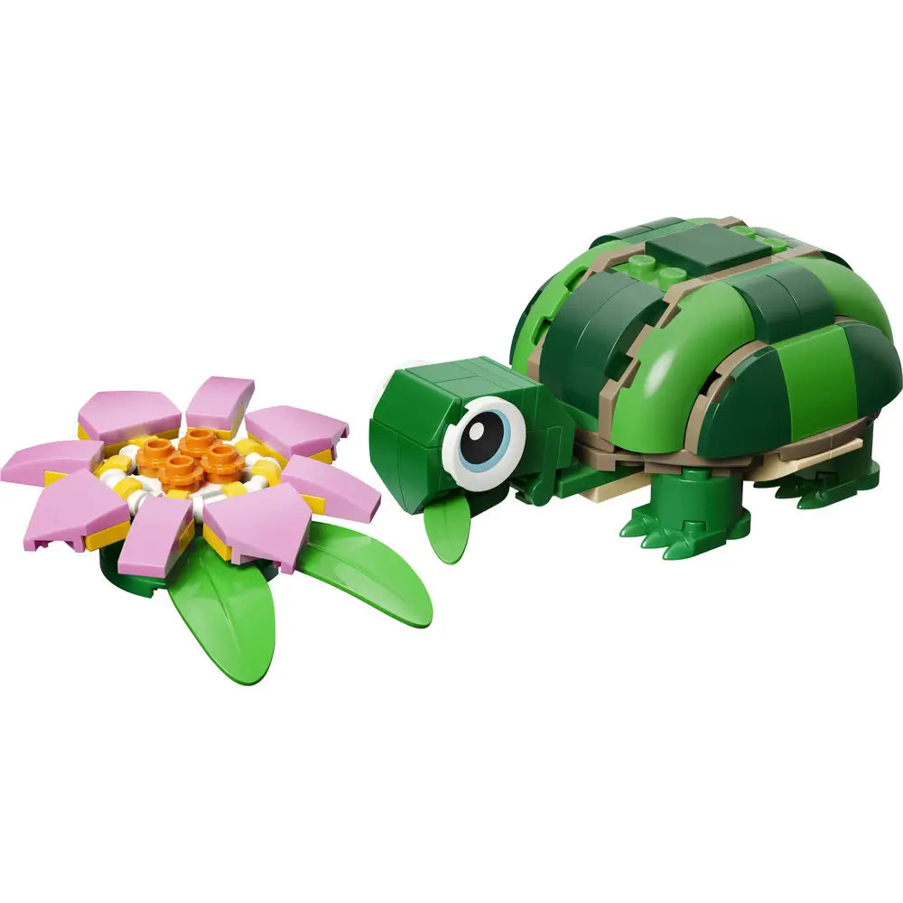 LEGO Creator turtle toy built from dark and light green plastic bricks with a smooth glossy texture, rounded shell shape, short legs, and large eye, positioned beside a pink water lily flower on a clean white background.