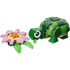 LEGO Creator turtle toy built from dark and light green plastic bricks with a smooth glossy texture, rounded shell shape, short legs, and large eye, positioned beside a pink water lily flower on a clean white background.