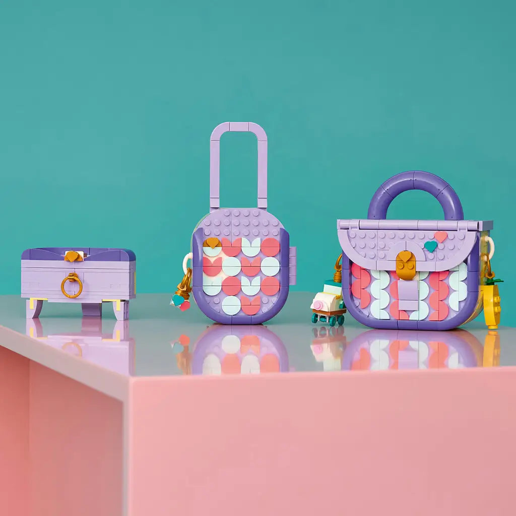 LEGO Creator Fashion Bag 3-in-1 builds in lavender, purple, coral and mint plastic, displaying a storage chest, tall bag and handbag with charms on a pink shelf against teal.