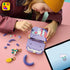 LEGO Creator Fashion Bag in lavender, purple, coral and mint plastic, as a child builds the open handbag among loose pieces, charms and digital instructions on a pink tabletop.