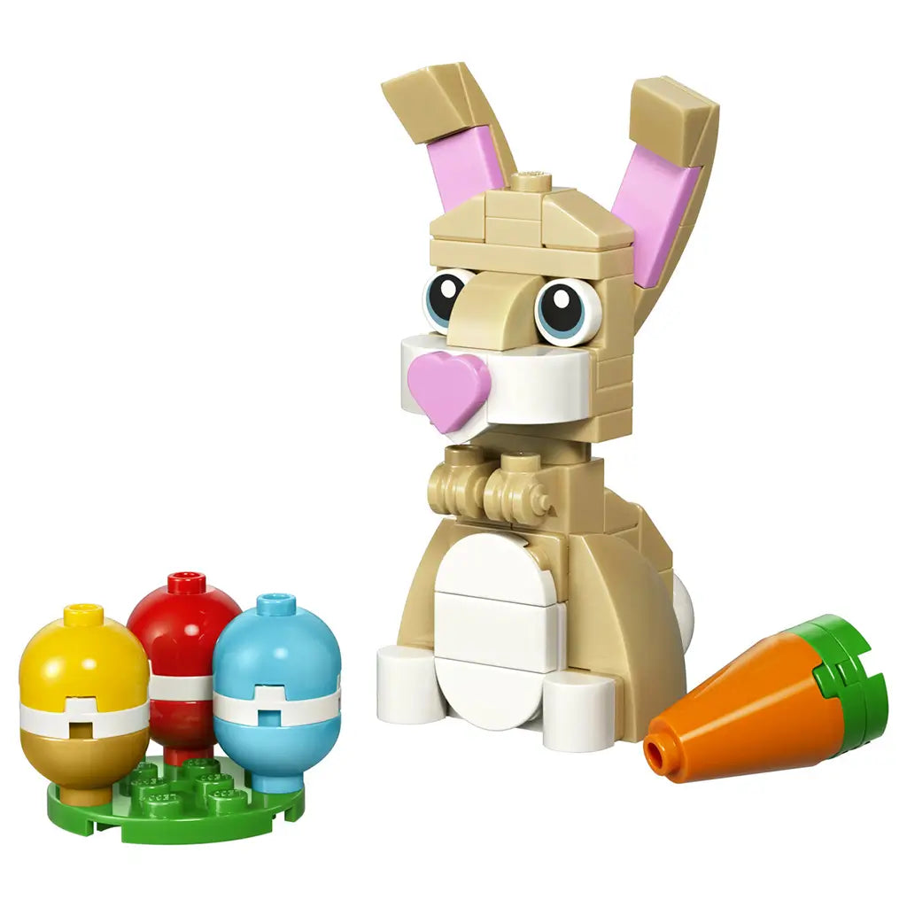 LEGO Creator Cute Easter Bunny toy display showing tan and white plastic bricks, smooth rounded bunny shape with tall pink-lined ears, large printed eyes, heart-shaped pink nose, colorful Easter eggs, and carrot accessory on white background.