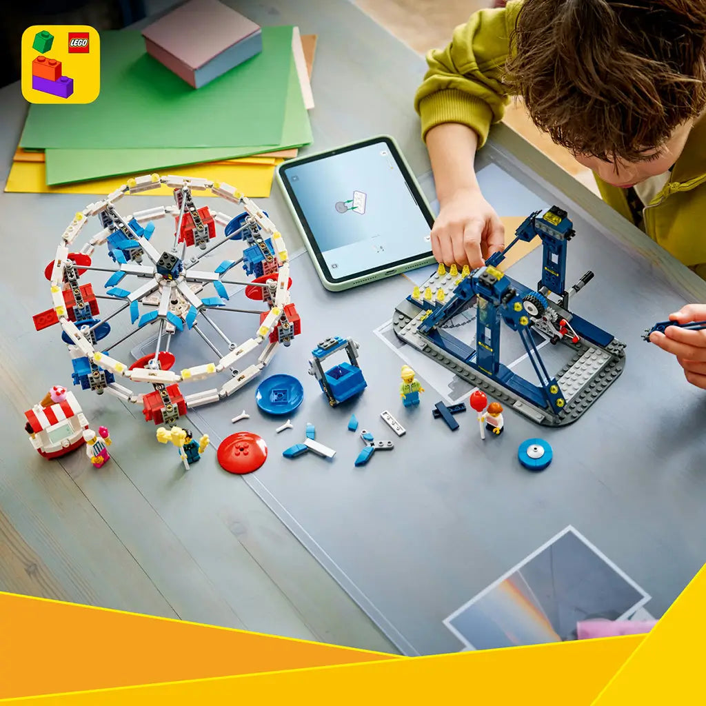 LEGO Creator Ferris Wheel in white, blue and red plastic, as a child builds the dark blue support frame beside the wheel, loose bricks, minifigures and a tablet.