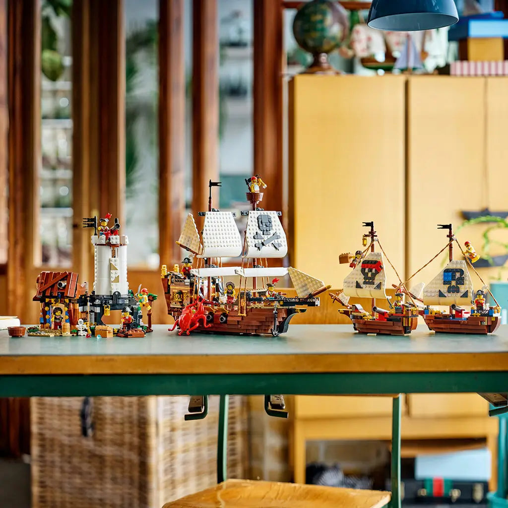LEGO Creator pirate builds in brown, white and black plastic, displaying a tall pirate hideout, large sailing ship and two smaller ships with minifigures on a table.