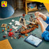 LEGO Creator pirate ship in brown, white and black plastic, as a child attaches a white sail while minifigures, a red sea monster, loose pieces and a tablet sit nearby.
