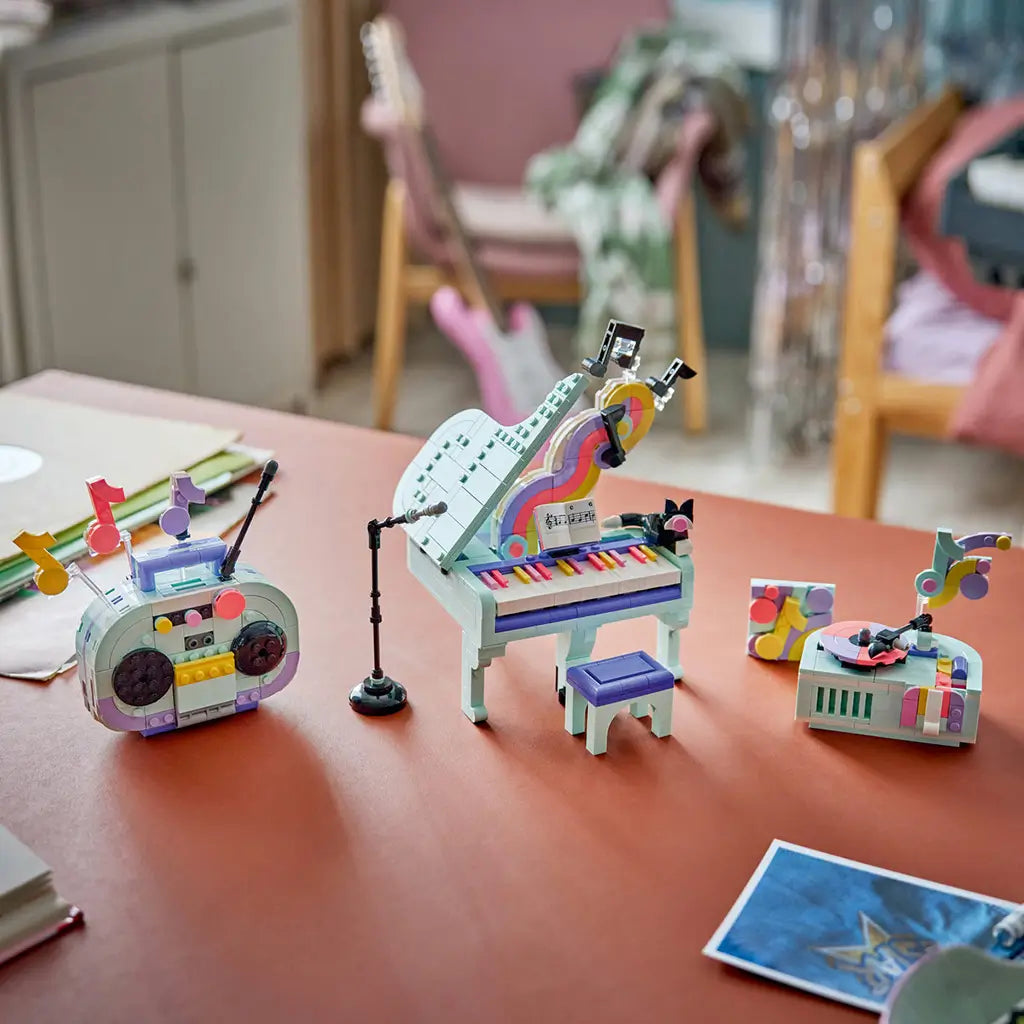 LEGO Creator Music Decor Piano 3-in-1 builds in mint, purple and pink plastic, displaying a grand piano, boombox and record player with music-note decorations on a table.