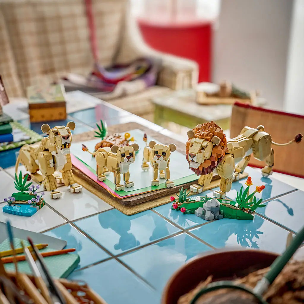LEGO Creator Majestic Lion models in tan, brown and green plastic, displaying a lion and three smaller wild cats with plant builds across a tiled craft table.