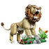 LEGO Creator Majestic Lion 31386 in tan and brown plastic, posed roaring beside a green habitat with gray rocks, grasses and colorful flowers on a white background.