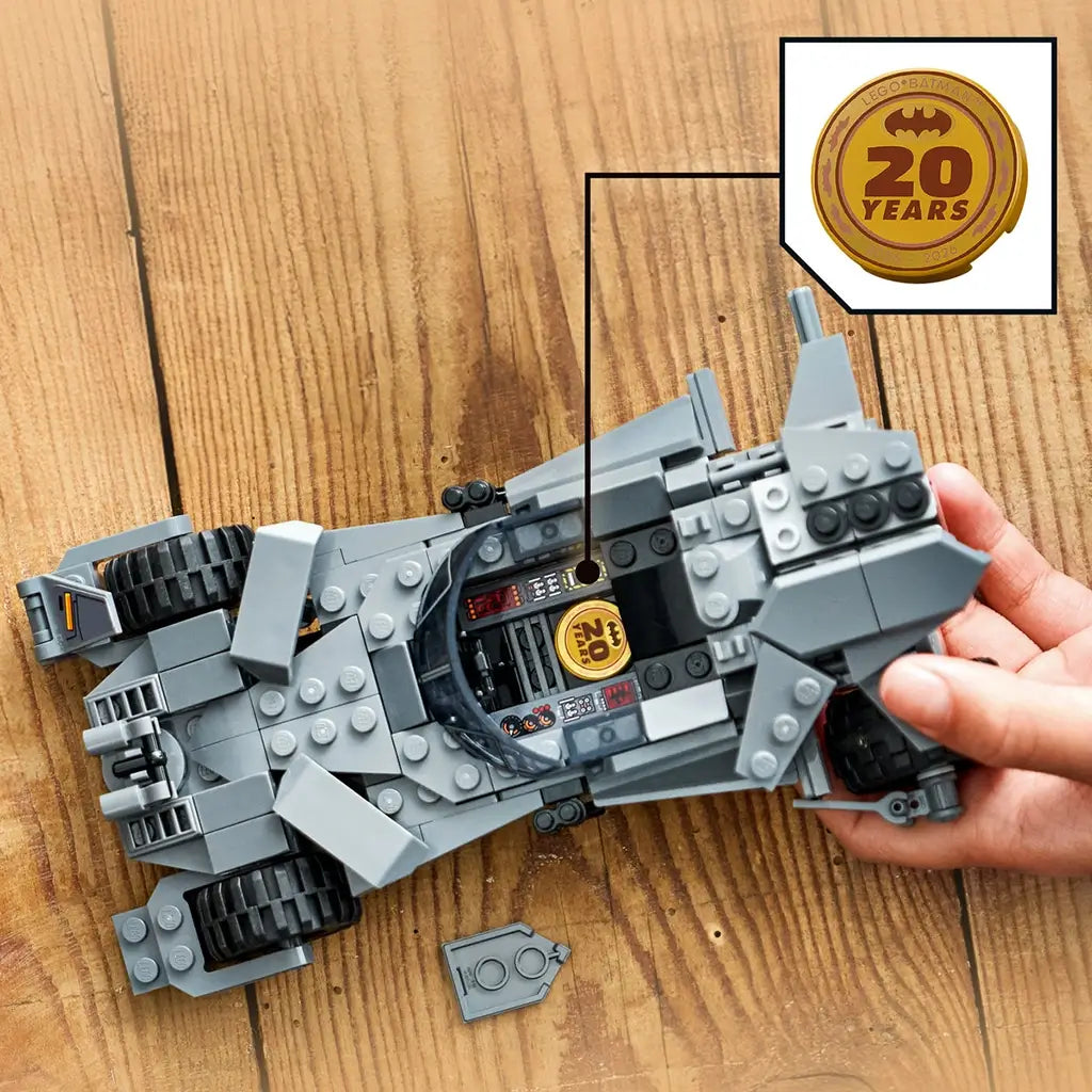 LEGO Batman Batmobile cockpit detail in gray plastic with angular panels and interior controls, open vehicle section revealing gold 20 years tile, close-up view on a wooden tabletop background.