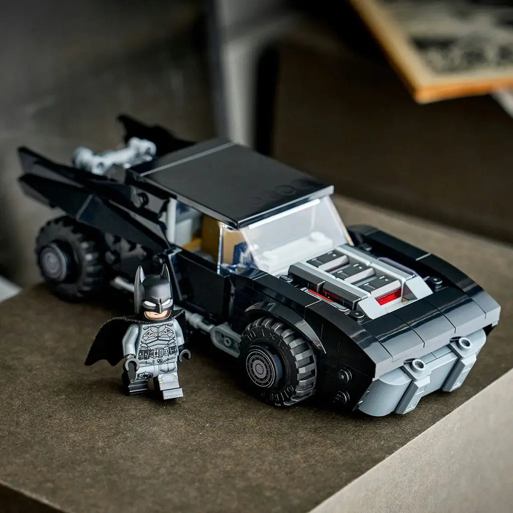 LEGO Batman Batmobile model in black plastic bricks, detailed hood engine and angular body shape, displayed with Batman minifigure on a dark surface with indoor background.