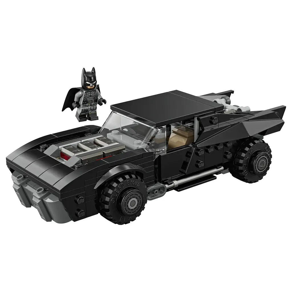 LEGO Batman Batmobile model in black plastic bricks, low wide muscle car shape with exposed engine detail, shown with Batman minifigure on a plain white background.