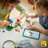 LEGO Disney Pixar Up building set in colorful plastic bricks, children assembling Kevin bird and Dug dog figures with tools and instruction tablet, creative play activity on a light tabletop.