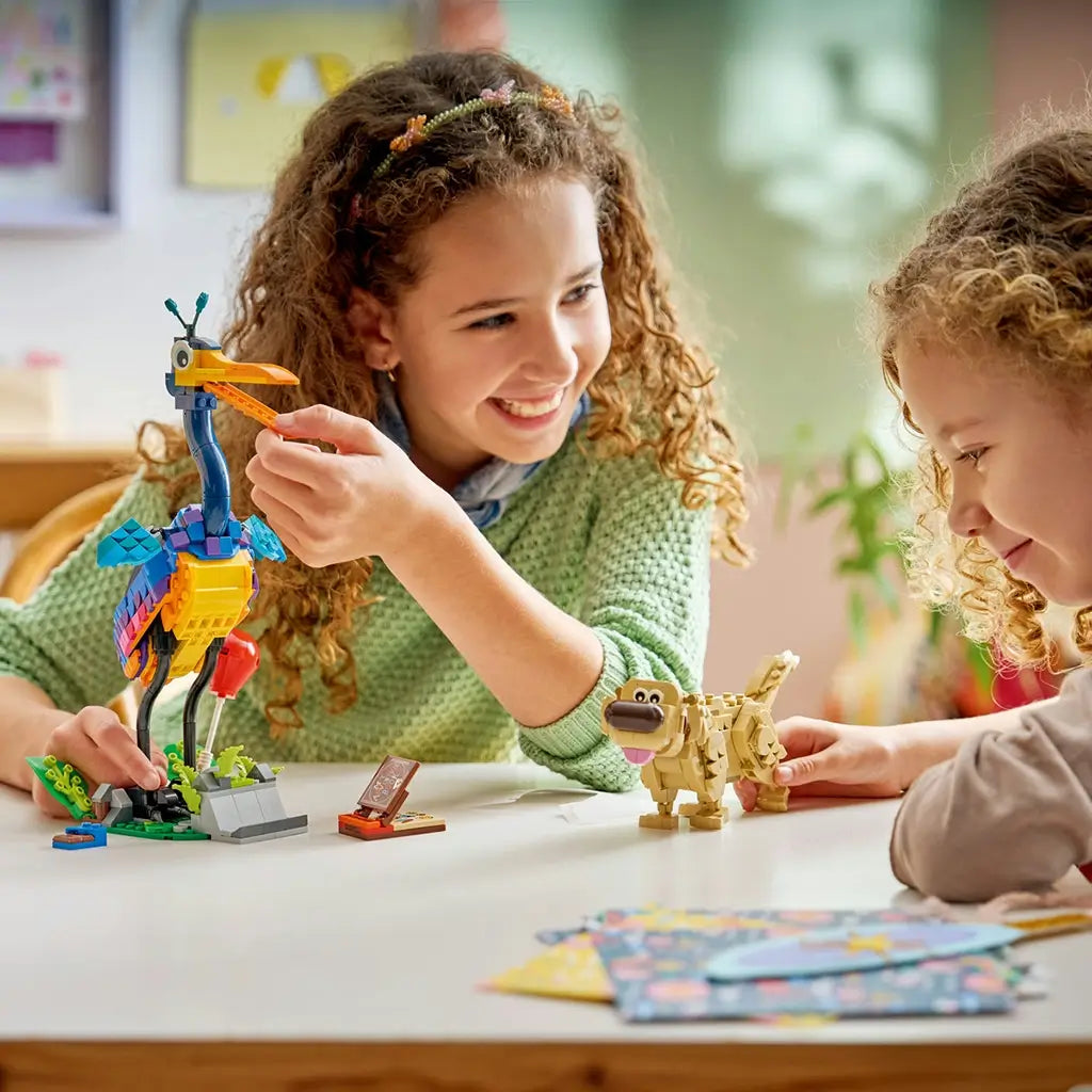 LEGO Disney Pixar Up Kevin and Dug build in colorful plastic, children interacting with tall bird figure and dog model, playful construction scene with accessories on a bright indoor table setting.
