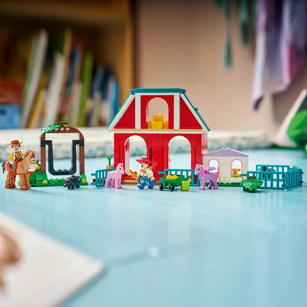 LEGO Disney Toy Story horse ranch display features red, teal and lavender plastic structures, fenced paddocks and animal figures arranged as a farm scene on a tabletop in a bedroom setting.