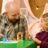 LEGO Disney Beach Fun with Lilo & Stitch set in blue, yellow, and tan plastic is played with by a child and adult at a green table in a cozy bedroom setting.