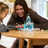 LEGO Disney Frozen ice castle playset displayed on a wooden table, icy blue and lavender tower with snowflake top, Anna, Elsa, and Olaf figures included, shown during interactive play between an adult and child indoors.
