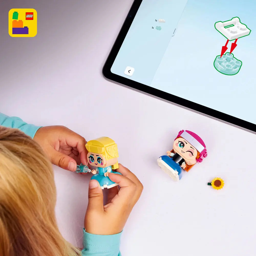 LEGO Disney Frozen Mini Anna and Elsa play scene showing a child assembling the small figures, with colorful plastic parts, sunflower and ice accessories, and digital building instructions displayed on a tablet nearby.