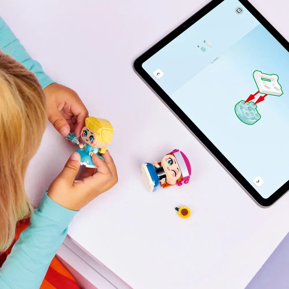 LEGO Disney Frozen Mini Anna and Elsa building activity shown on a tabletop, with small plastic figure parts, bright accessories, and a tablet displaying step-by-step digital instructions during assembly.