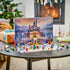 LEGO Disney Princess Advent Calendar 2026 display features colorful plastic figures, animals, a Christmas tree, train and castle tower on a snowy mat beside a glowing fireplace.